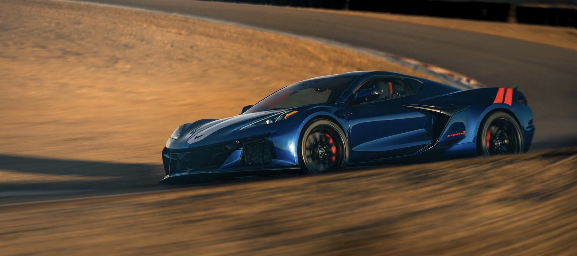 2027 Chevrolet Corvette Grand Sport in blue on racetrack banking, dynamic side view with orange stripes