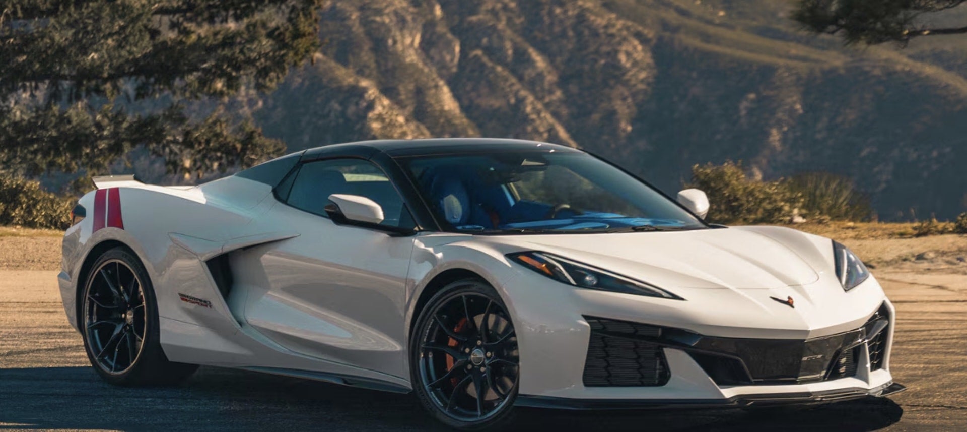2027 Chevrolet Corvette Grand Sport in white, front three-quarter view in the mountains with black roof and red stripe