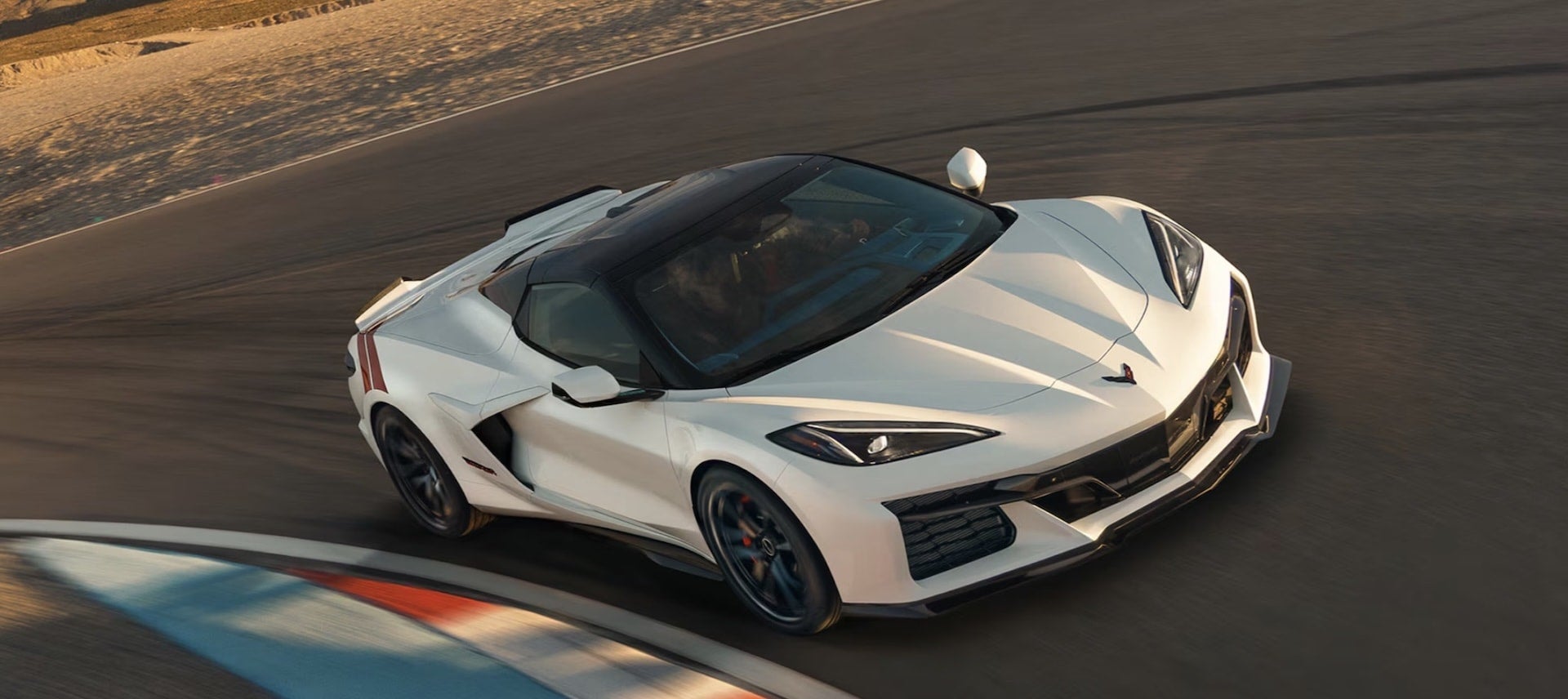 2027 Chevrolet Corvette Grand Sport in white, overhead front three-quarter view on a racetrack with red side stripe