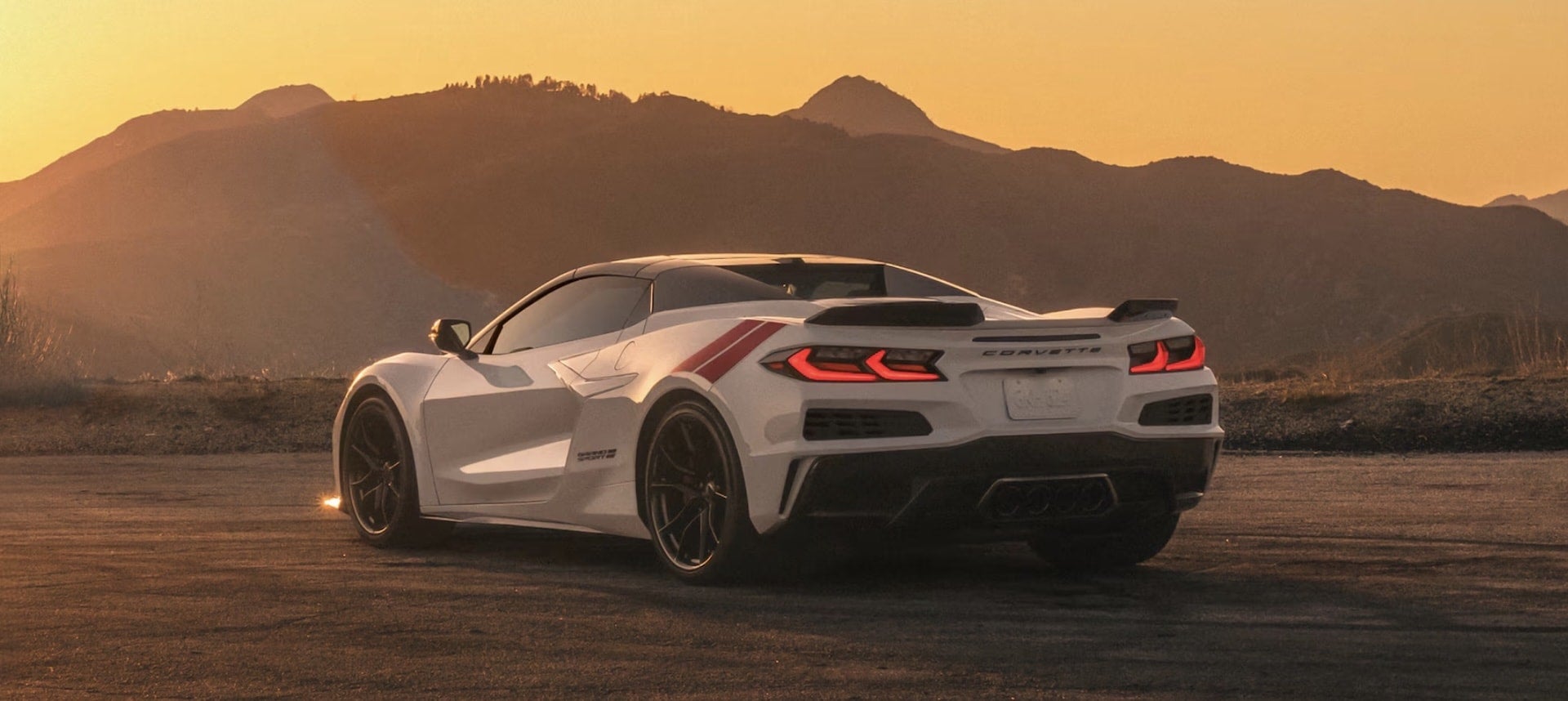 2027 Chevrolet Corvette Grand Sport in white, rear three-quarter view at sunset with red racing stripe